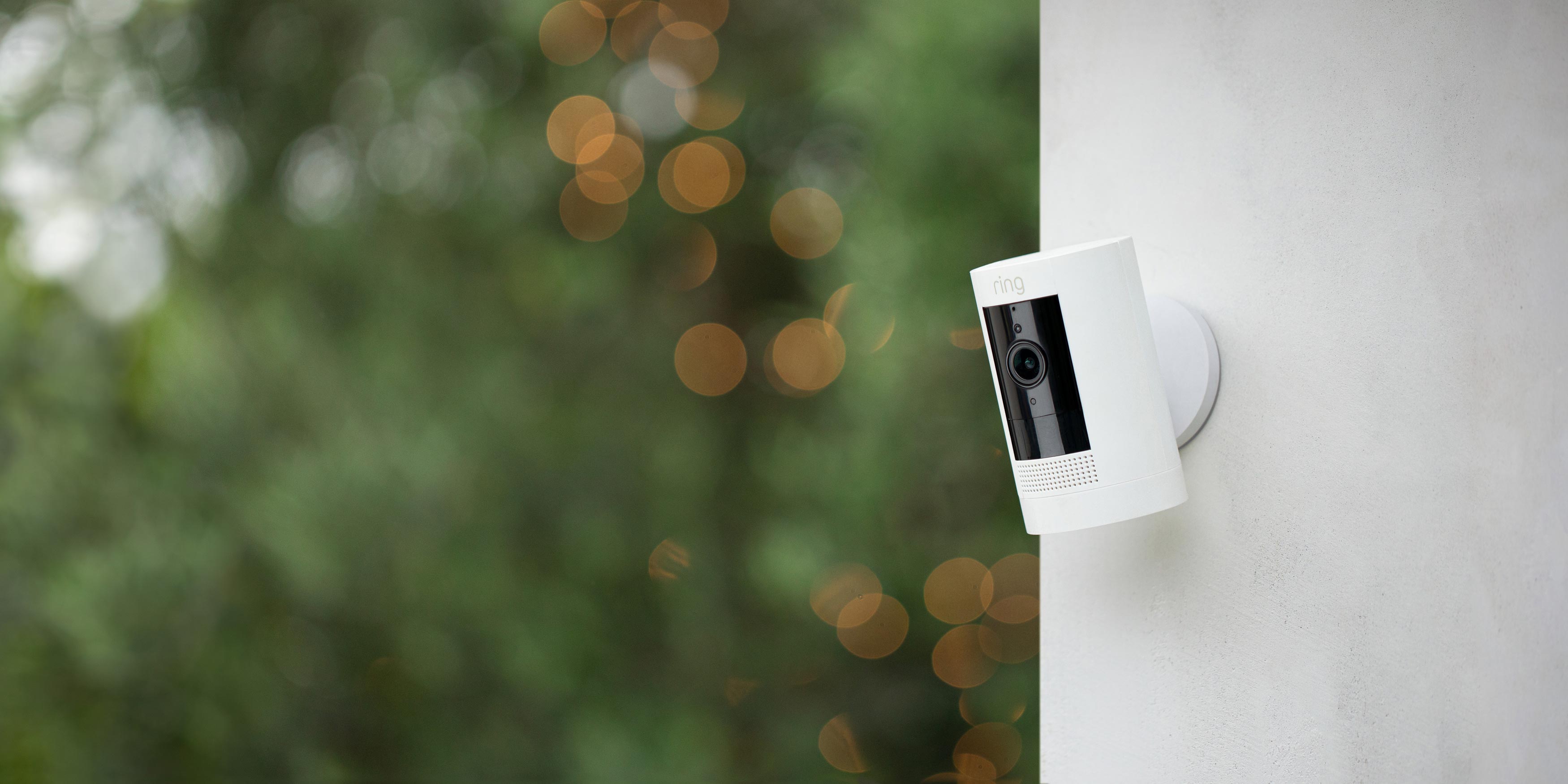 Ring camera mounted on an exterior white wall in front of greenery in the background