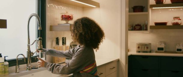 child  filling up a cup of water in a nice kitchen with strip lighting